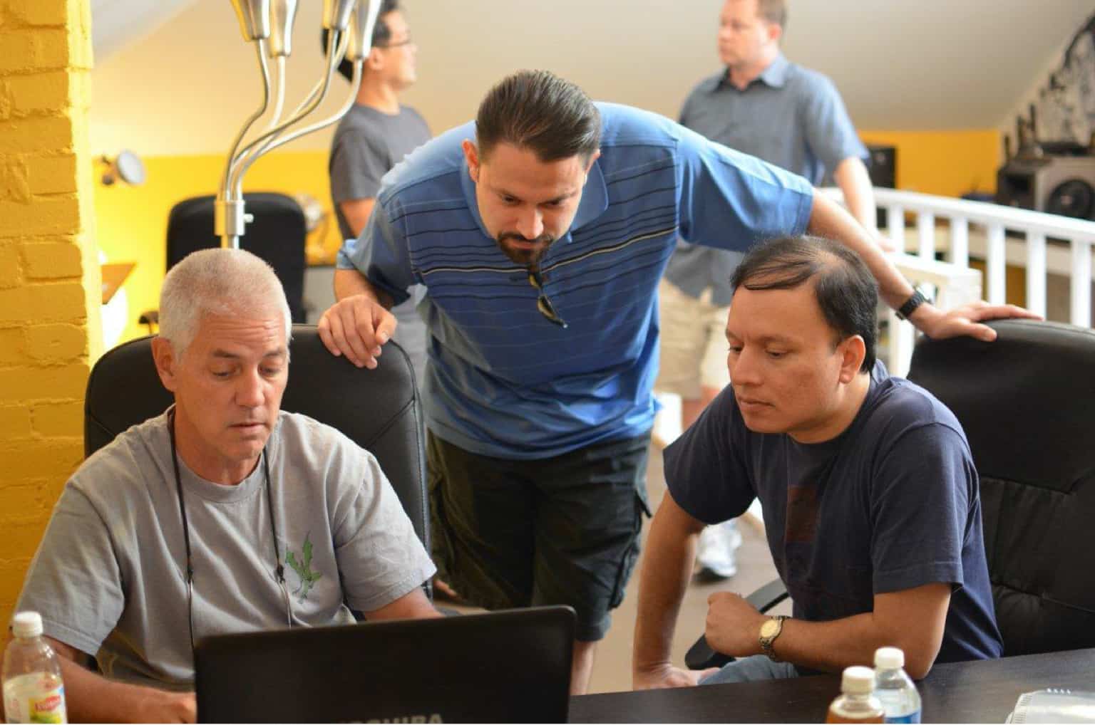 Richard, Andres, and Bijal gathered around a desk looking at a laptop computer screen.